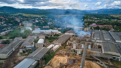 Drone shot of a large industrial complex with warehouse buildings, rising steam and silos beside a small town