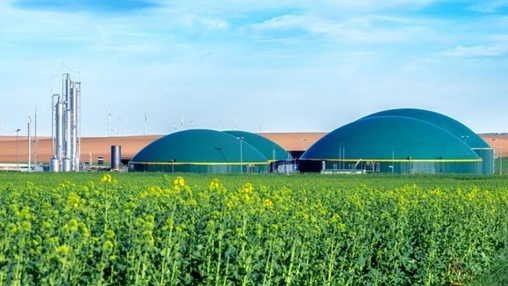 Green domed anaerobic digesters at a biogas plant with flowering crops and wind turbines on the horizon