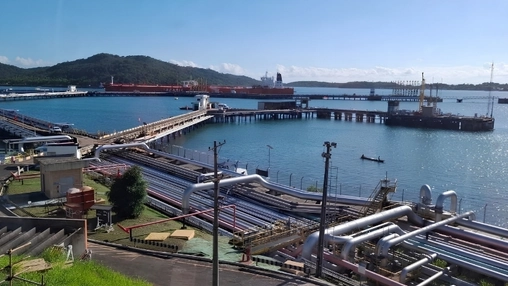 Industrial port with large pipeline infrastructure, loading jetties, and a tanker vessel at the terminal