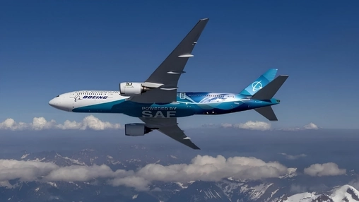 Boeing aircraft in flight with Powered by SAF livery over snow-capped mountains and a blue sky with clouds