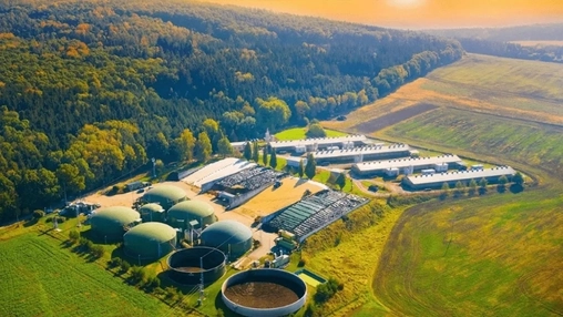 Aerial view of a bioenergy facility with green biogas domes surrounded by agricultural fields and forest