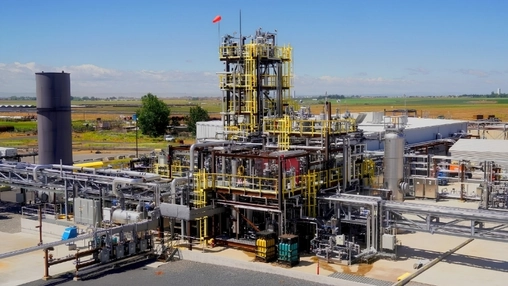Industrial plant with a red-flagged tower, yellow scaffolding, and interconnected silver pipe systems