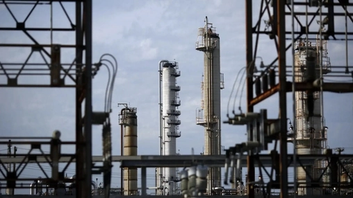 Industrial refinery distillation towers viewed through steel framework structures against a cloudy sky